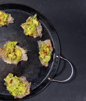 Top view of delicious pork rinds with guacamole on traditional comal. Tasty avocado sauce on fried pork snacks above round griddle. Authentic Mexican food
