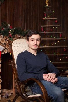 A young guy sits on an armchair by the fireplace