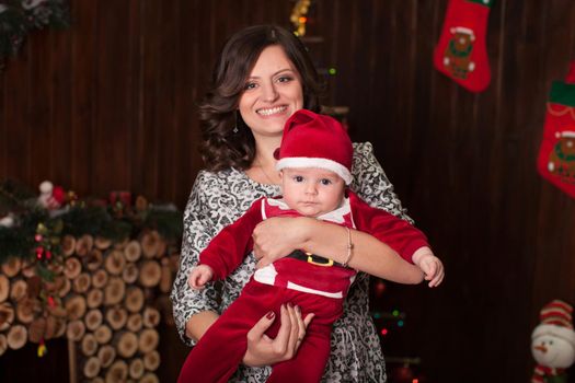 Mom and son in Santa Claus costume in a home setting near a fireplace in front of a wooden wall
