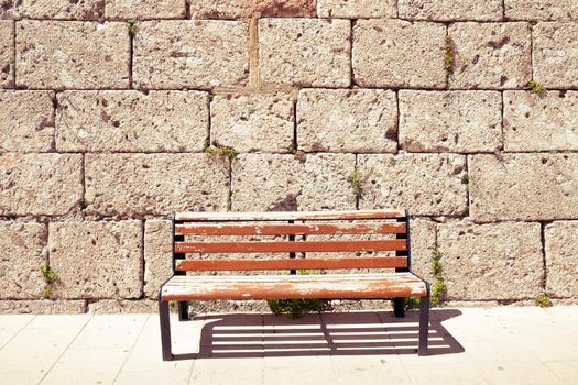 old weathered red bench close to stone wall 