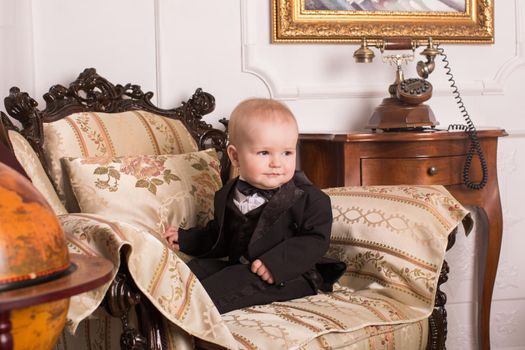 Child in a tuxedo sitting in an office talking on the phone.