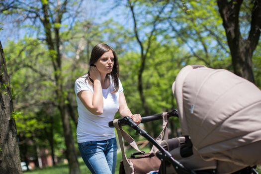 Young mother walking and pushing a stroller in the park