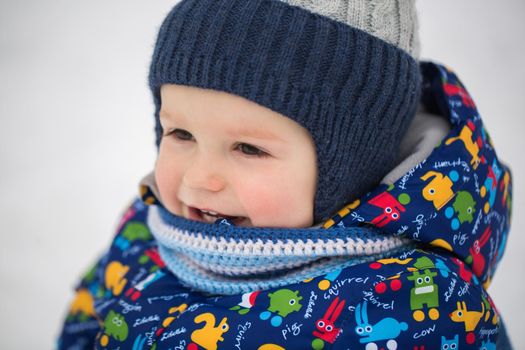 A little boy in a winter jacket is sitting in the snow