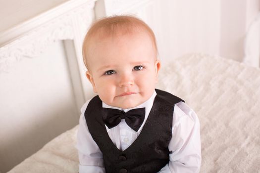 Child in a tuxedo, sitting on the bed next to the fireplace. The groom.