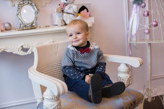 The little boy in the red tie sitting in a chair in the new year interior.