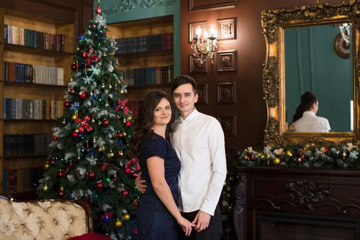 Man and woman holding hands near Christmas tree and fireplace in the Christmas atmosphere.