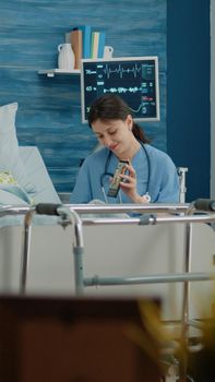 Senior woman talking to family on video call conference with help from nurse in nursing home. Old patient with disease and medical assistant using smartphone for remote communication