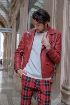 beautiful guy with red leather jacket and backpack in the center of reggio emilia. High quality photo