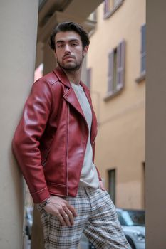 beautiful guy with red leather jacket and backpack in the center of reggio emilia. High quality photo