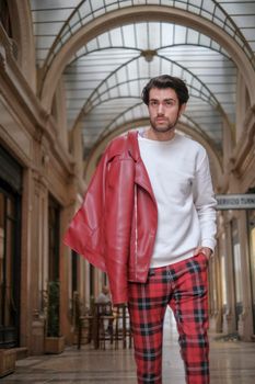 beautiful guy with red leather jacket and backpack in the center of reggio emilia. High quality photo