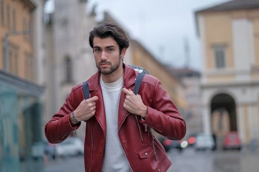 beautiful guy with red leather jacket and backpack in the center of reggio emilia. High quality photo