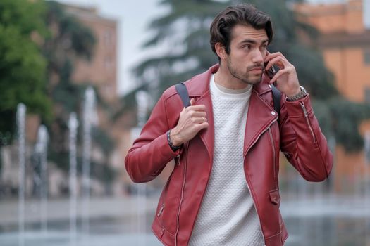 beautiful guy with red leather jacket and backpack in the center of reggio emilia. High quality photo