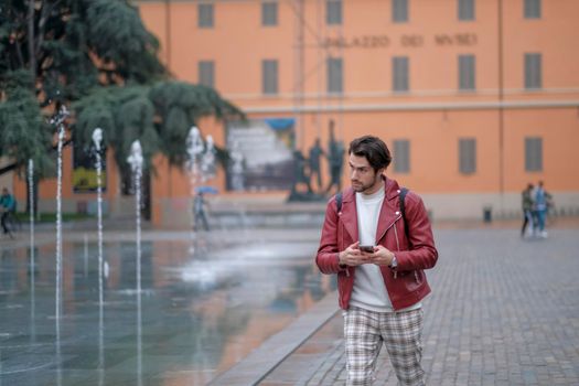 beautiful guy with red leather jacket and backpack in the center of reggio emilia. High quality photo