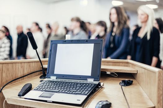 Laptop and microphone on rostrum in lecture hall full of conference participants. Business and entrepreneurship symposium.