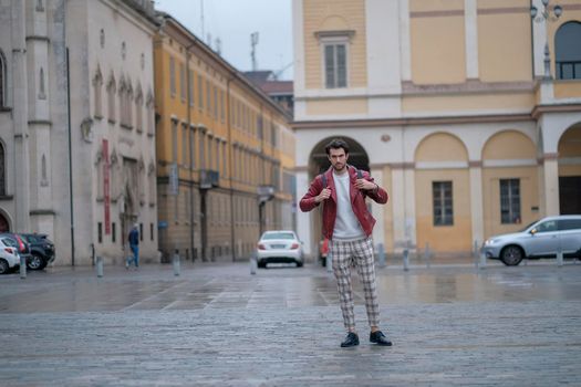 beautiful guy with red leather jacket and backpack in the center of reggio emilia. High quality photo