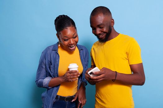 Modern couple looking at smartphone and enjoying laugh together. Cheerful lovers having fun with technology on mobile phone and browsing internet. People in relationship using telephone.