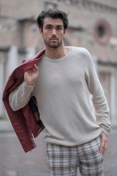 beautiful guy with red leather jacket and backpack in the center of reggio emilia. High quality photo