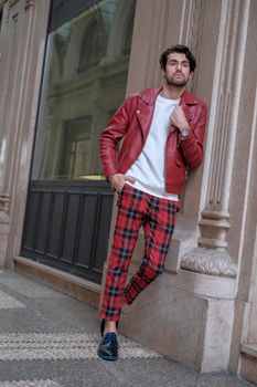 beautiful guy with red leather jacket and backpack in the center of reggio emilia. High quality photo