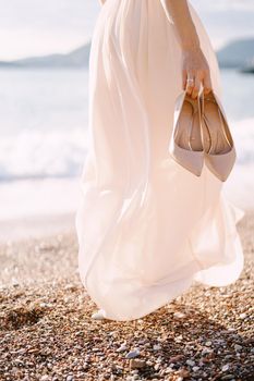Bride with high-heeled shoes in her hand walks along the beach. Close-up. High quality photo
