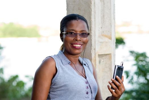 young woman smiling with a mobile phone and leaning against an electric pole outside ..