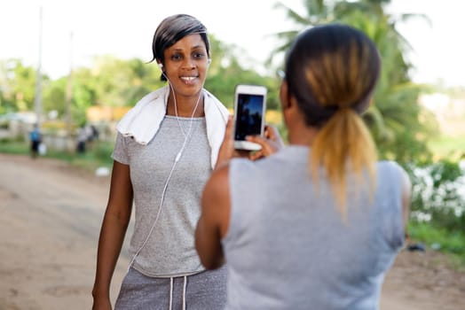 young woman standing photographing her friend after sport with mobile phone.