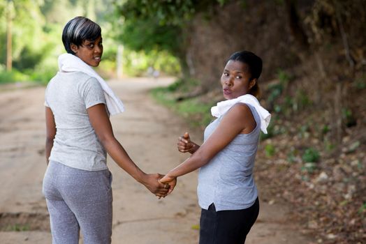two happy women in sportswear walking back while holding hands outdoors in the park