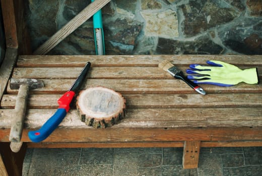 an old hammer, a hand saw, protective gloves and a round pine beam with sawdust on a bench. Wooden stand for food for the master class. DIY concept.