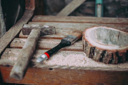 an old rusty hammer, a paint brush and a round pine beam with sawdust on a bench. Wooden stand for food for the master class. DIY concept.