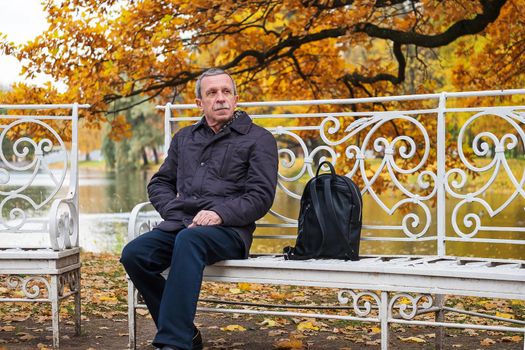 Close-up portrait of adult man. Boarder sits on a bench in a beautiful park near pond. Rest, relaxation, slowdown in nature in golden autumn. Selective focus.