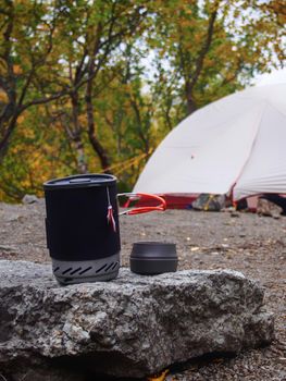 A pot for a gas burner with a mug sits on a stone against the background of a tent. photo