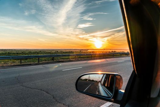 Evening trip to travel on the highway by car at sunset sunrise in the golden hour. Heavenly light.Dramatic evening sky with clouds and rays of the sun view from the window.Panoramic view of clouds