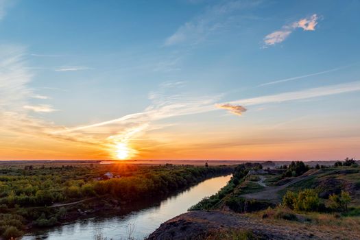 The heavenly light of the sun over the river and the forest.Dramatic evening sky with clouds and rays of the sun.Golden hour at evening sunset or morning sunrise.Panoramic view of cirrus clouds