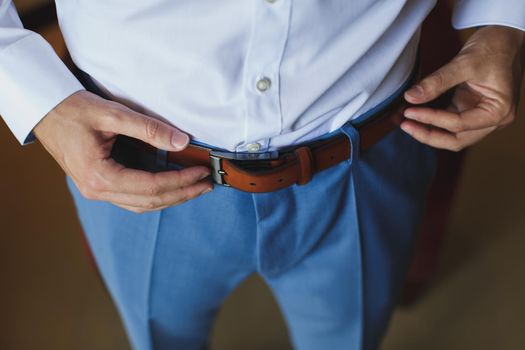 Man corrects belt, fees groom, man's hands, dressing, man buttons pants, jeans