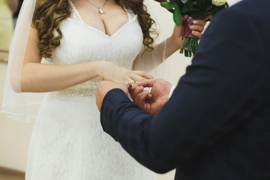 Newlyweds exchange rings, groom puts the ring on the bride's hand in marriage registry office