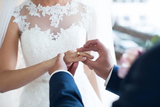 The groom puts a ring on the bride's finger during the wedding ceremony