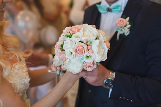 Groom in a suit gives the bride a white and peach wedding bouquet