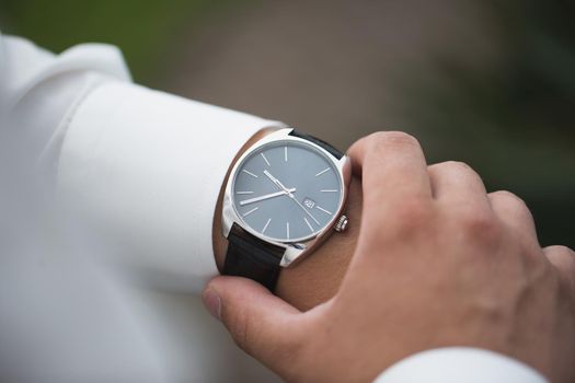Close up of businessman looking at watch on his hand outdoors, free space. Man in white shirt checking time from luxury wristwatches. Watch on hand. Groom wedding preparation
