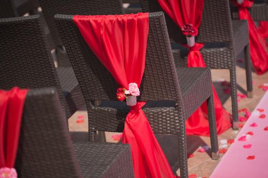 Row of wedding chairs decorated with red roses.