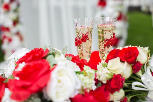 The champagne glasses. Wedding ceremony outdoors. Bouquet with red flowers.