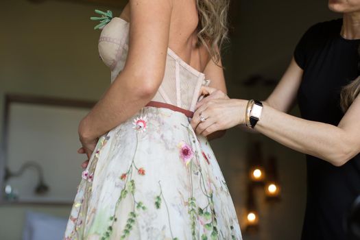 A woman helps the bride to put on a wedding dress