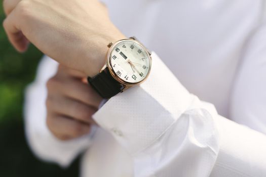 Close-up hands of the groom with a clock