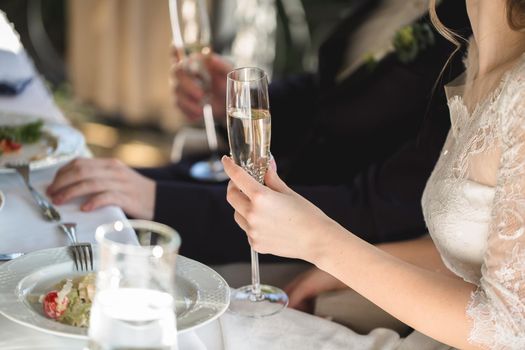 The bride and groom hold crystal glasses filled with champagne