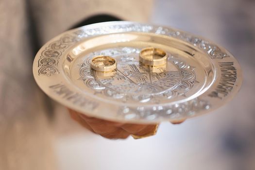 Wedding rings on a gold platter in the hands of a priest
