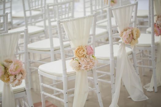 wedding decorations flowers on chairs. Wedding exit registration, white chairs decorated for wedding. wedding setup detail.