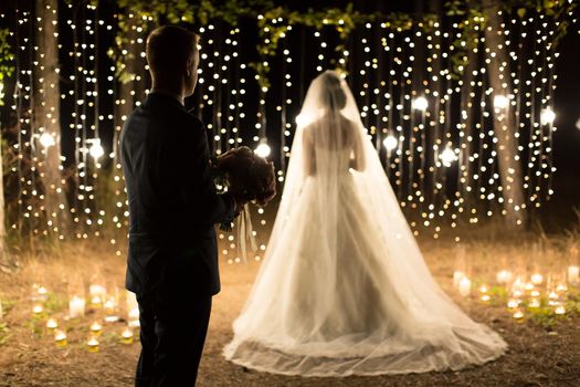 Wedding ceremony night. Meeting of the newlyweds, the bride and groom in the coniferous pine forest of candles and light bulbs.