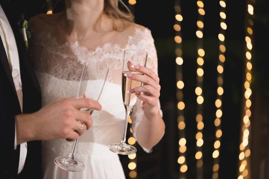 The bride and groom hold crystal glasses filled with champagne