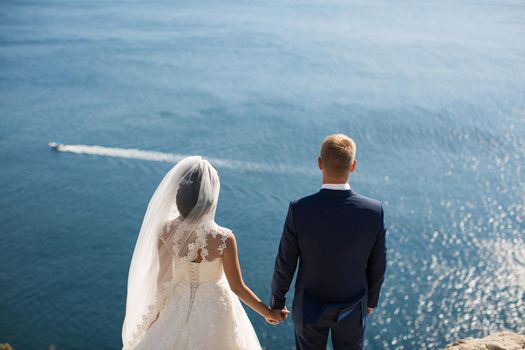 Bride and groom holding hands on a cliff against the sea.
