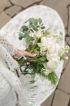 Delicate bouquet of white peonies in the hands of the bride on the background of the train of the wedding dress.