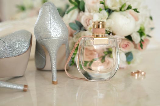 Silver shoes of the bride , perfume, bouquet and wedding rings on the dressing table near the mirror