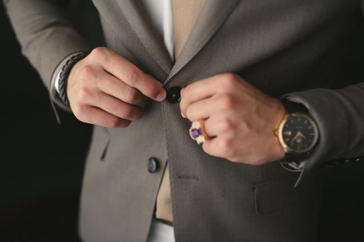 A man puts on a wedding suit and fastens a button.